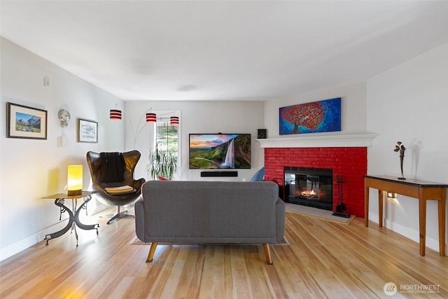 living area featuring light wood finished floors, a brick fireplace, and baseboards