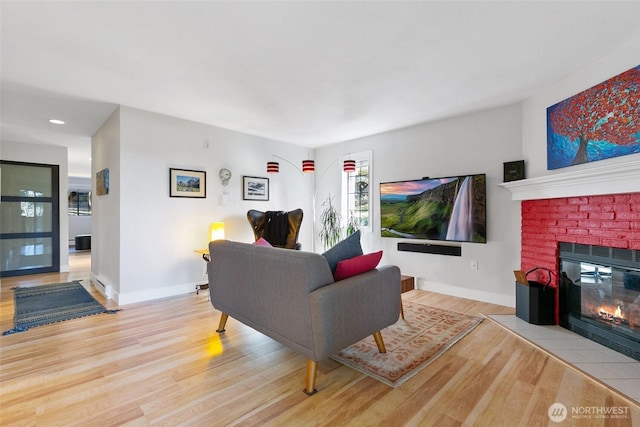 living room featuring a brick fireplace, baseboards, and wood finished floors