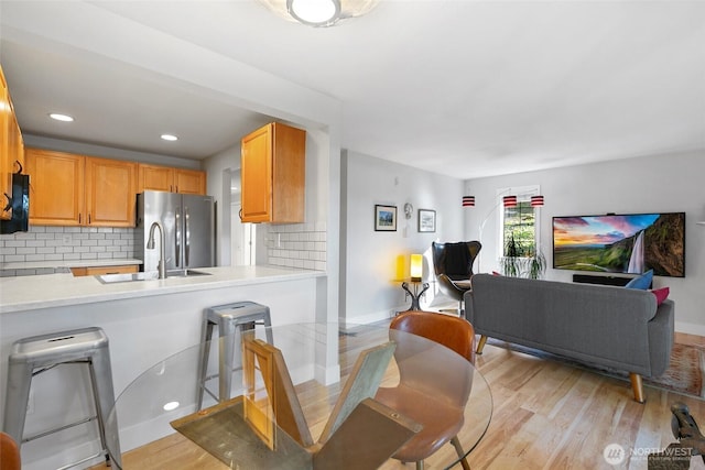 interior space featuring a sink, light countertops, light wood-type flooring, freestanding refrigerator, and tasteful backsplash