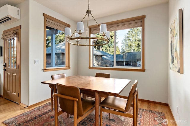 dining area with light wood-type flooring, an AC wall unit, baseboards, and an inviting chandelier