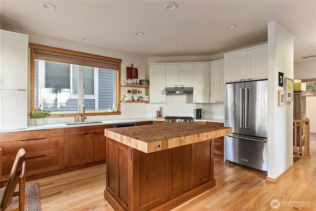 kitchen featuring butcher block counters, a kitchen island, a sink, under cabinet range hood, and high end refrigerator