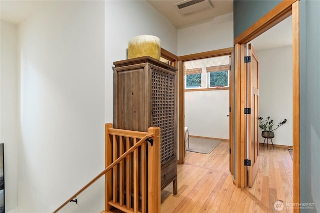 hallway featuring light wood-style flooring, visible vents, and an upstairs landing