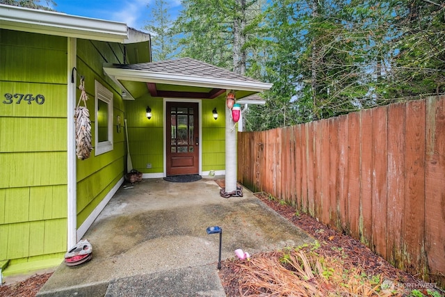 doorway to property with a shingled roof and fence