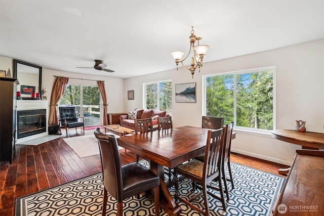 dining room with a fireplace with flush hearth, light wood-style floors, baseboards, and ceiling fan with notable chandelier