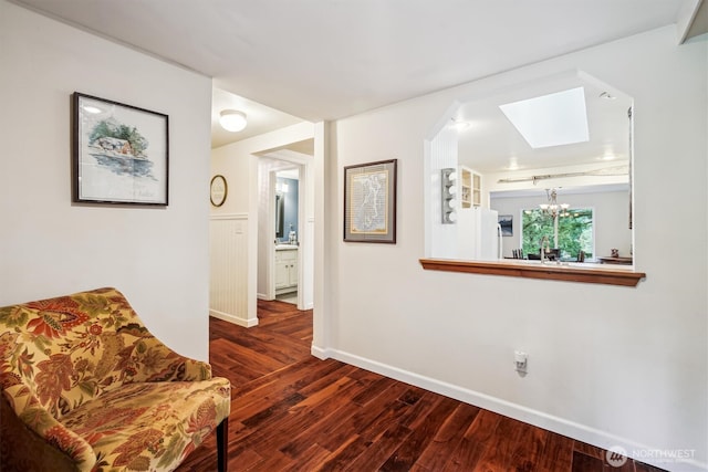 sitting room with a chandelier, a skylight, dark wood finished floors, and baseboards