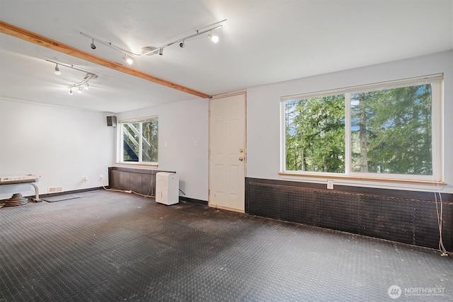 empty room featuring dark colored carpet, visible vents, track lighting, brick wall, and baseboards