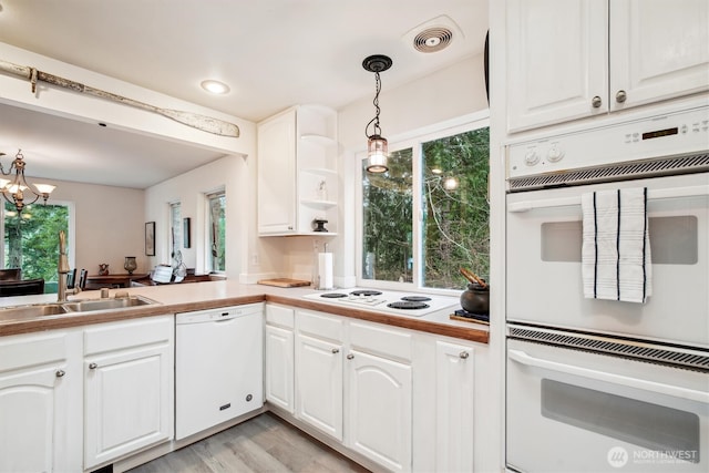 kitchen featuring white appliances, white cabinetry, hanging light fixtures, and a sink