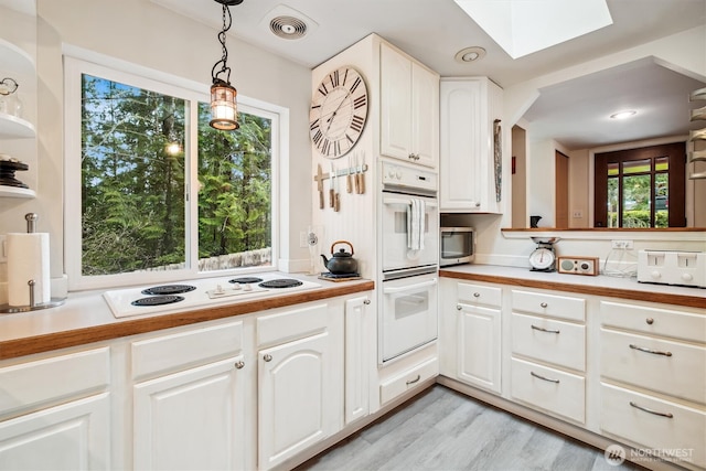 kitchen with a skylight, pendant lighting, visible vents, white cabinetry, and white appliances