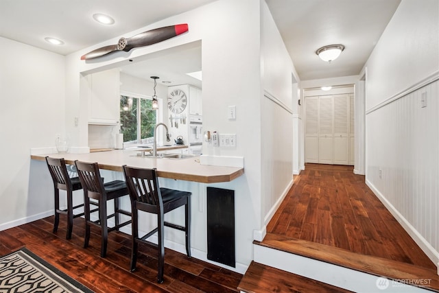 kitchen with light countertops, white cabinets, a sink, a peninsula, and a kitchen breakfast bar