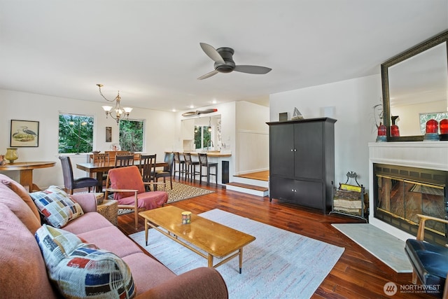 living room featuring dark wood-style floors, ceiling fan with notable chandelier, and a fireplace with flush hearth