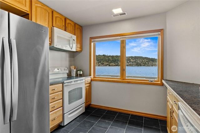 kitchen with dark countertops, a water view, visible vents, white appliances, and baseboards