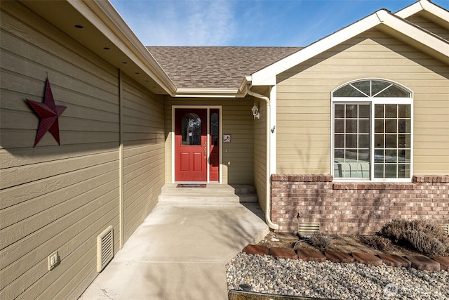 view of exterior entry with visible vents, a shingled roof, crawl space, and brick siding