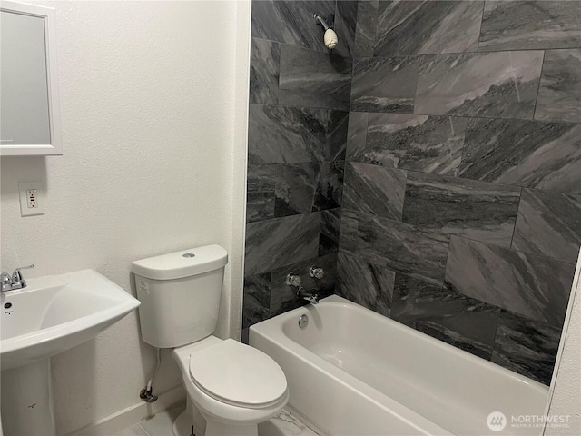 bathroom with a textured wall, tub / shower combination, a sink, and toilet