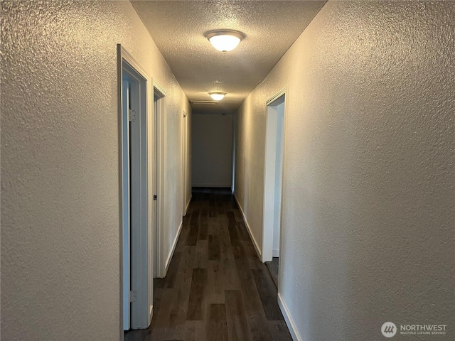 hallway featuring a textured ceiling, a textured wall, dark wood-style floors, and baseboards