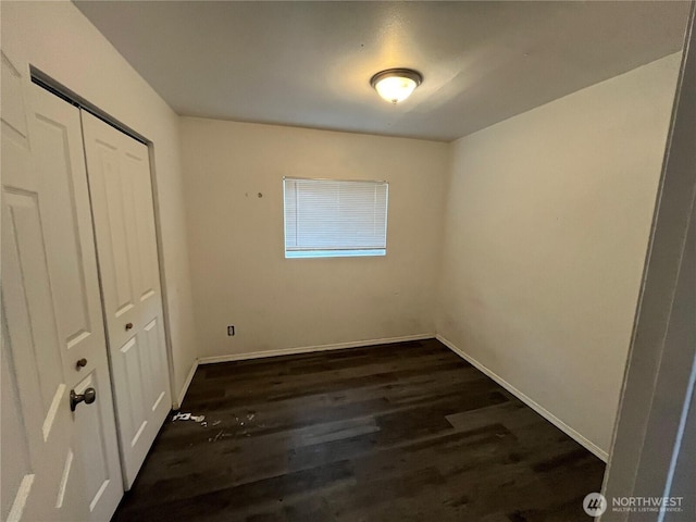 unfurnished bedroom with baseboards, dark wood-type flooring, and a closet