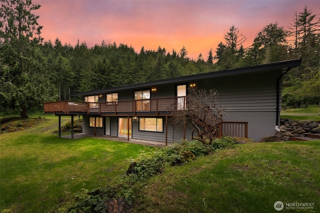 back of house at dusk featuring a deck and a lawn