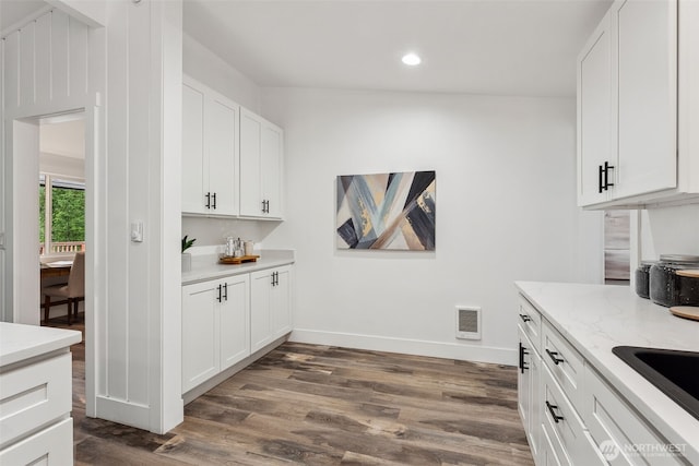 kitchen with a sink, visible vents, white cabinets, light stone countertops, and dark wood finished floors