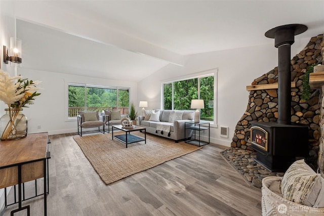 living room featuring lofted ceiling with beams, wood finished floors, visible vents, a wealth of natural light, and a wood stove