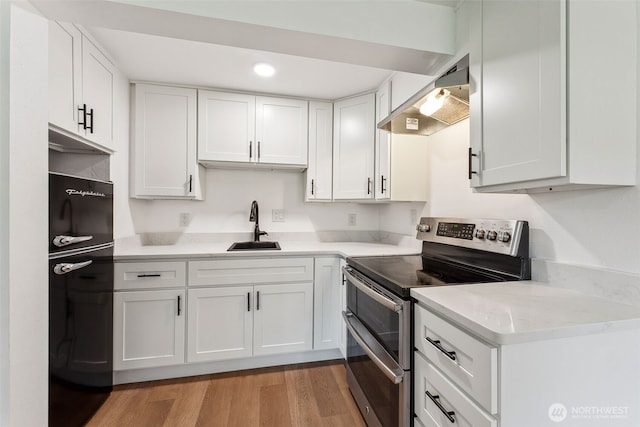 kitchen with range with two ovens, white cabinetry, a sink, and ventilation hood