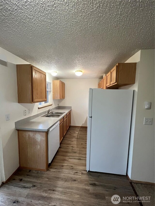 kitchen featuring a textured ceiling, white appliances, wood finished floors, a sink, and light countertops