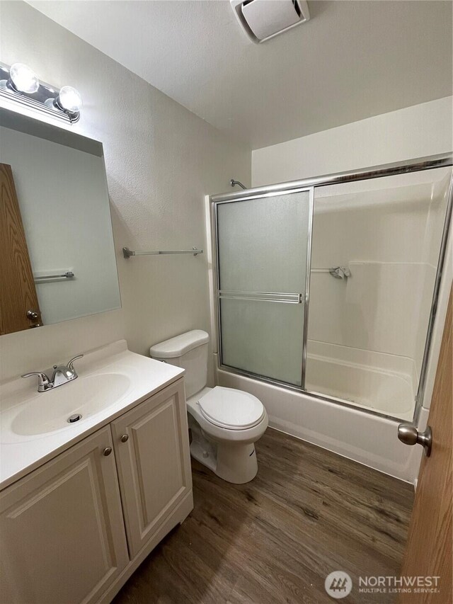 bathroom with enclosed tub / shower combo, toilet, wood finished floors, vanity, and visible vents