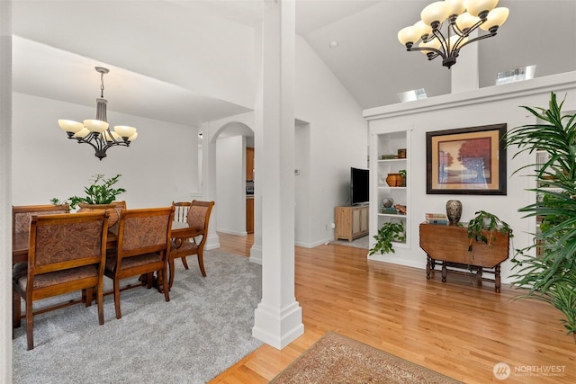 dining area with built in shelves, a chandelier, light wood-style flooring, arched walkways, and high vaulted ceiling