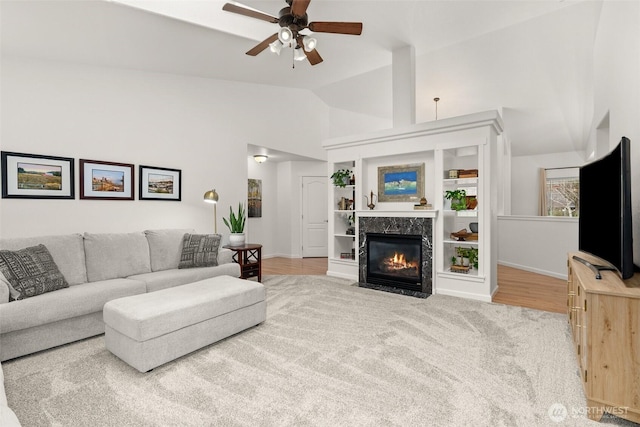 living area featuring a premium fireplace, baseboards, high vaulted ceiling, and ceiling fan