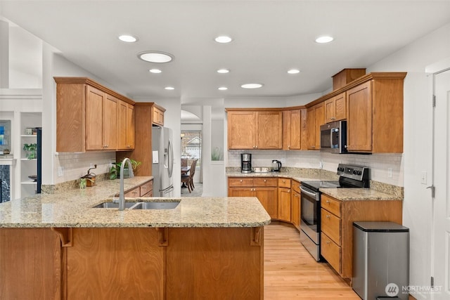 kitchen featuring light stone counters, a peninsula, stainless steel appliances, and a sink