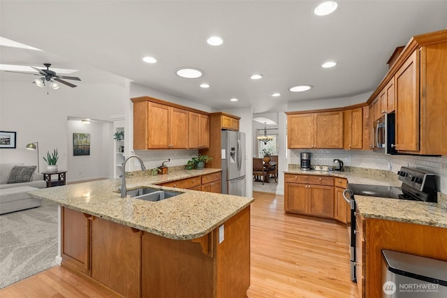 kitchen with light stone counters, a peninsula, stainless steel appliances, a sink, and open floor plan