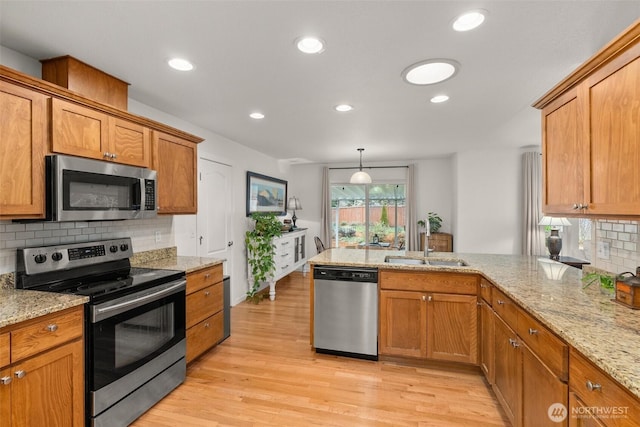 kitchen with a sink, stainless steel appliances, light wood-style flooring, and brown cabinetry