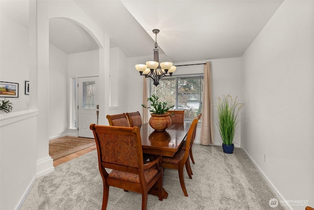 dining room featuring arched walkways, a notable chandelier, light colored carpet, and baseboards