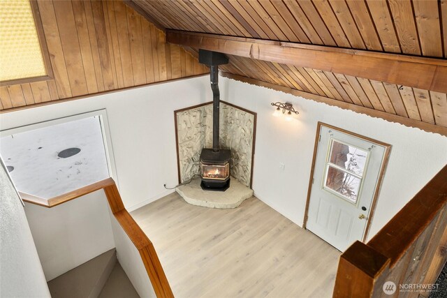 unfurnished living room with vaulted ceiling with beams, wooden ceiling, light wood finished floors, and a wood stove