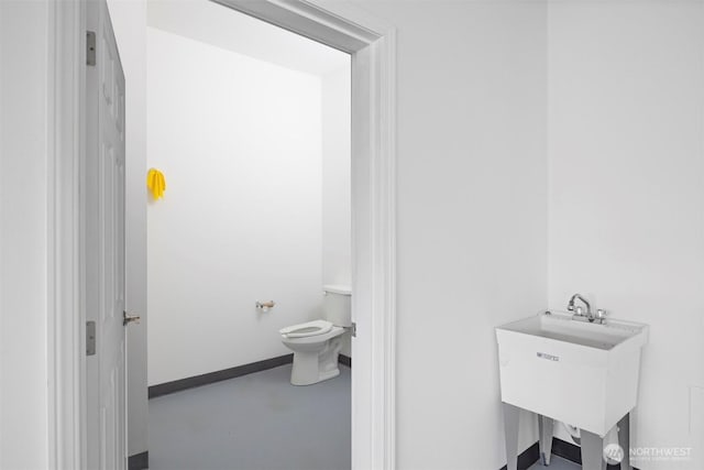 bathroom with finished concrete flooring, a sink, toilet, and baseboards