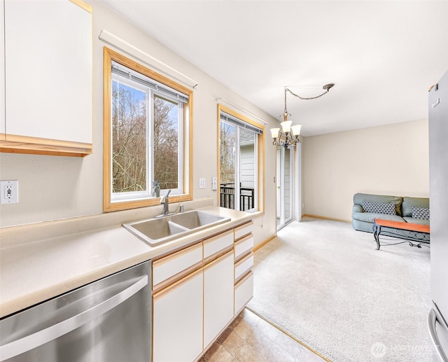 kitchen with a sink, white cabinets, light countertops, stainless steel dishwasher, and hanging light fixtures