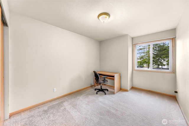 unfurnished office with light colored carpet, a textured ceiling, and baseboards