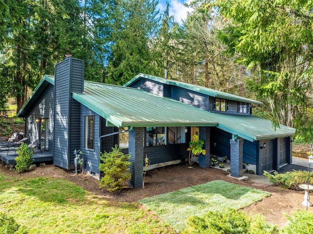 mid-century inspired home with a garage, a chimney, metal roof, a deck, and a front yard