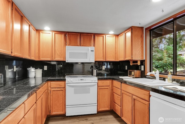 kitchen featuring white appliances, a sink, light wood-type flooring, backsplash, and recessed lighting