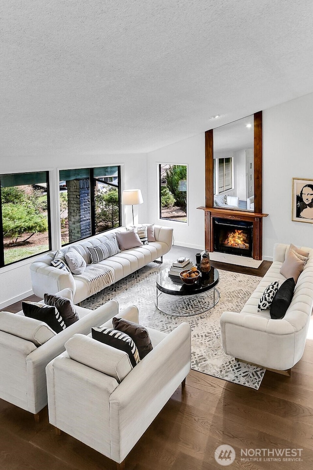 living area with a warm lit fireplace, a textured ceiling, wood finished floors, and baseboards