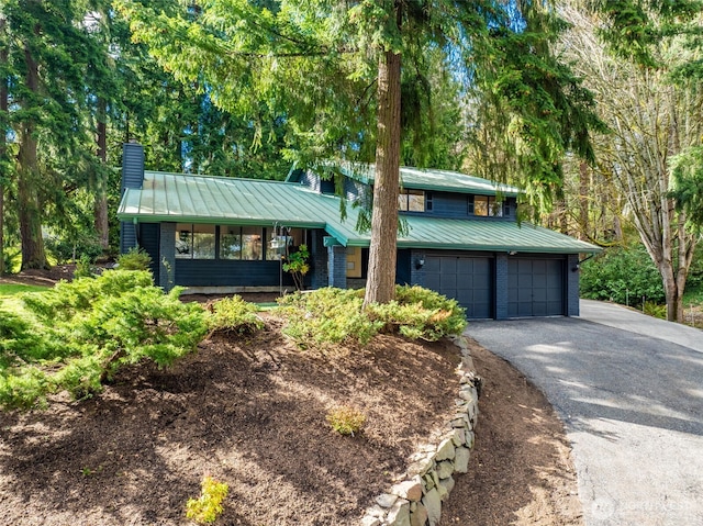 split level home with metal roof, aphalt driveway, brick siding, a standing seam roof, and a chimney