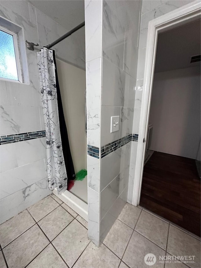 bathroom featuring tile patterned floors, visible vents, tile walls, and a stall shower