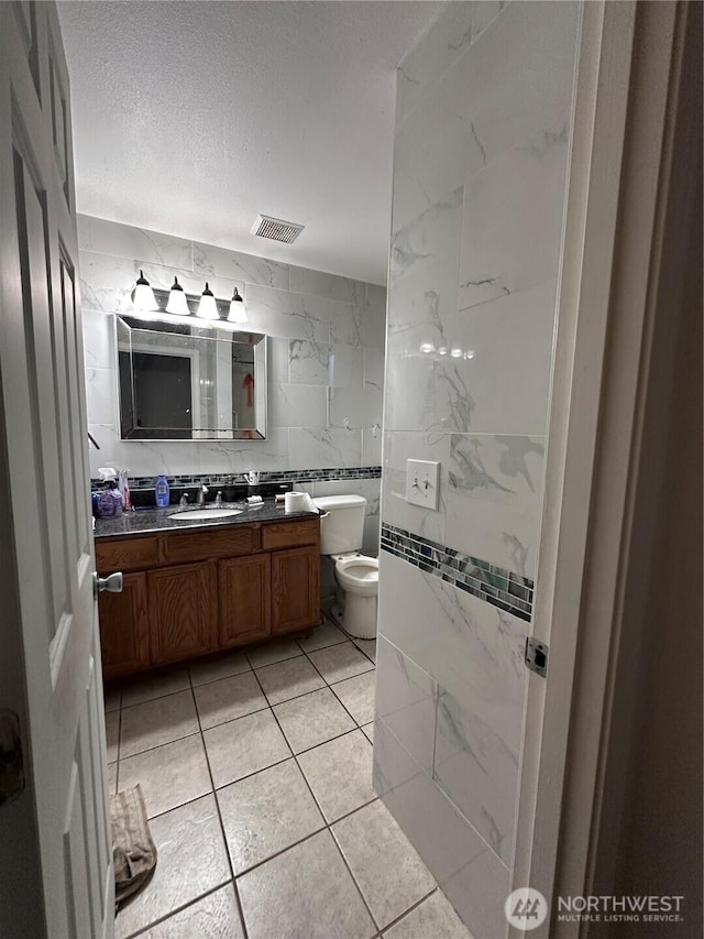 bathroom featuring visible vents, toilet, a textured ceiling, tile walls, and vanity