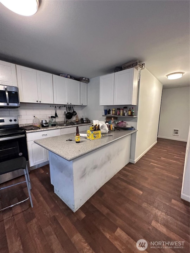 kitchen with backsplash, appliances with stainless steel finishes, white cabinets, light stone countertops, and dark wood-style flooring