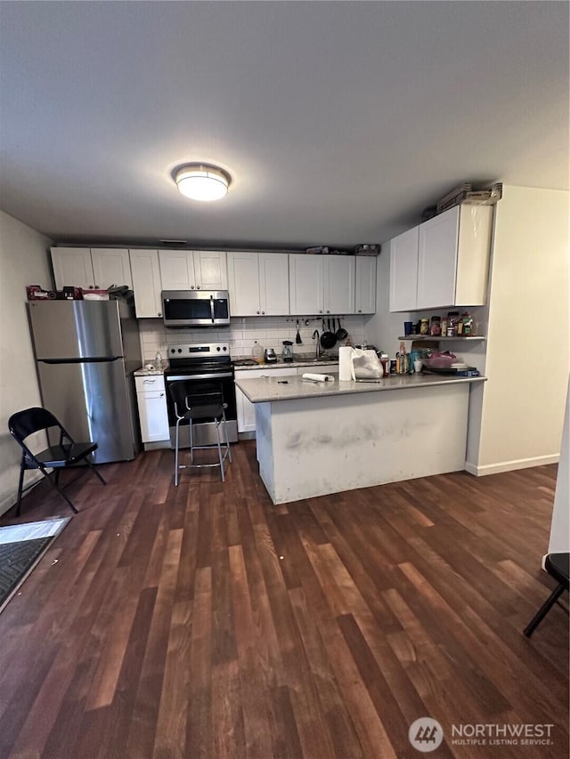 kitchen with a peninsula, tasteful backsplash, dark wood-style flooring, and stainless steel appliances