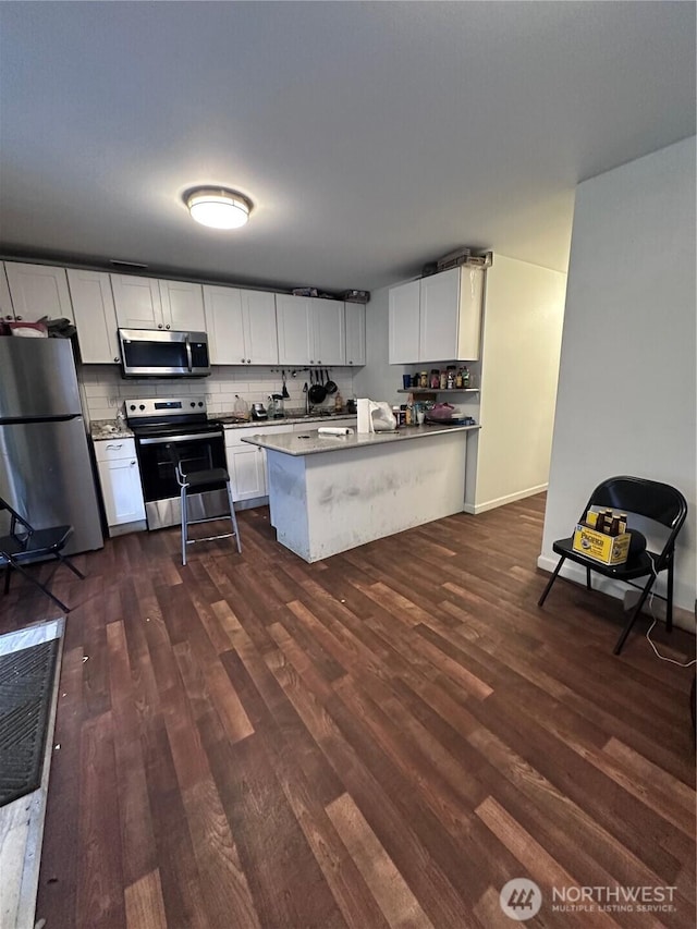 kitchen with backsplash, white cabinetry, a peninsula, stainless steel appliances, and dark wood-style flooring