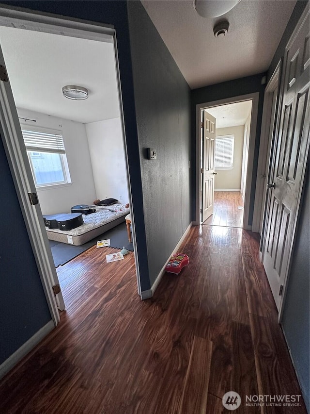 corridor featuring wood finished floors, baseboards, and a textured ceiling