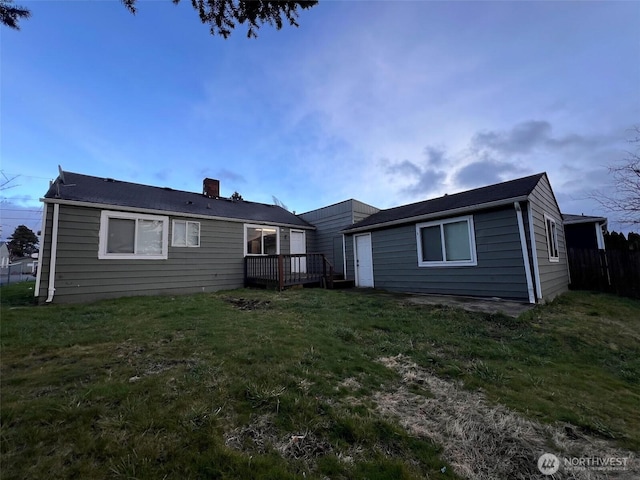 back of property with a lawn, a chimney, and a wooden deck