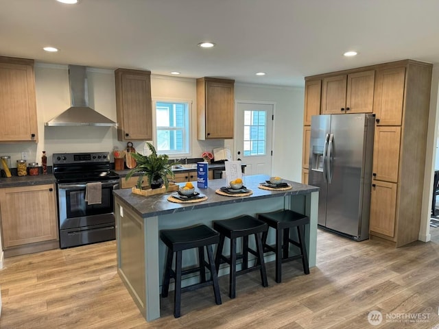 kitchen with dark countertops, wall chimney exhaust hood, appliances with stainless steel finishes, a center island, and a kitchen bar