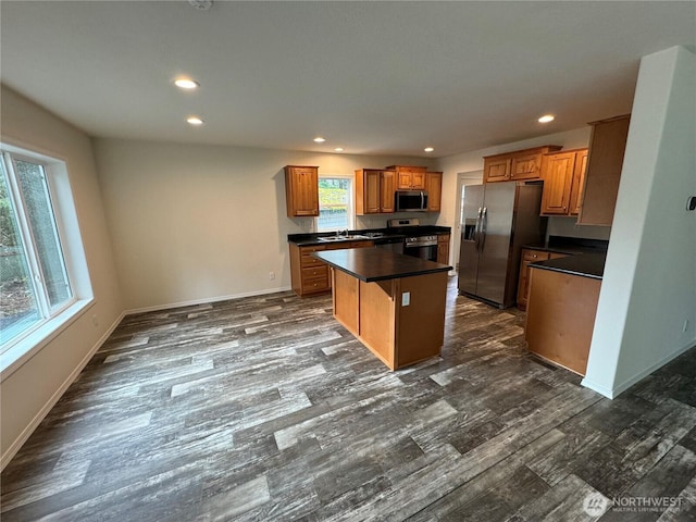 kitchen featuring dark countertops, a kitchen island, appliances with stainless steel finishes, brown cabinets, and dark wood-type flooring