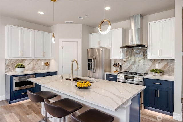 kitchen featuring appliances with stainless steel finishes, a sink, light wood-style floors, blue cabinetry, and wall chimney exhaust hood