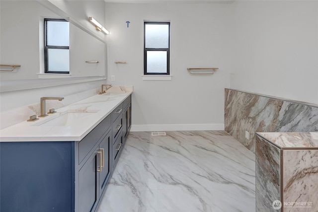 full bath with double vanity, a sink, marble finish floor, and baseboards